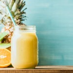 Freshly blended yellow and orange fruit smoothie in glass jar with straw